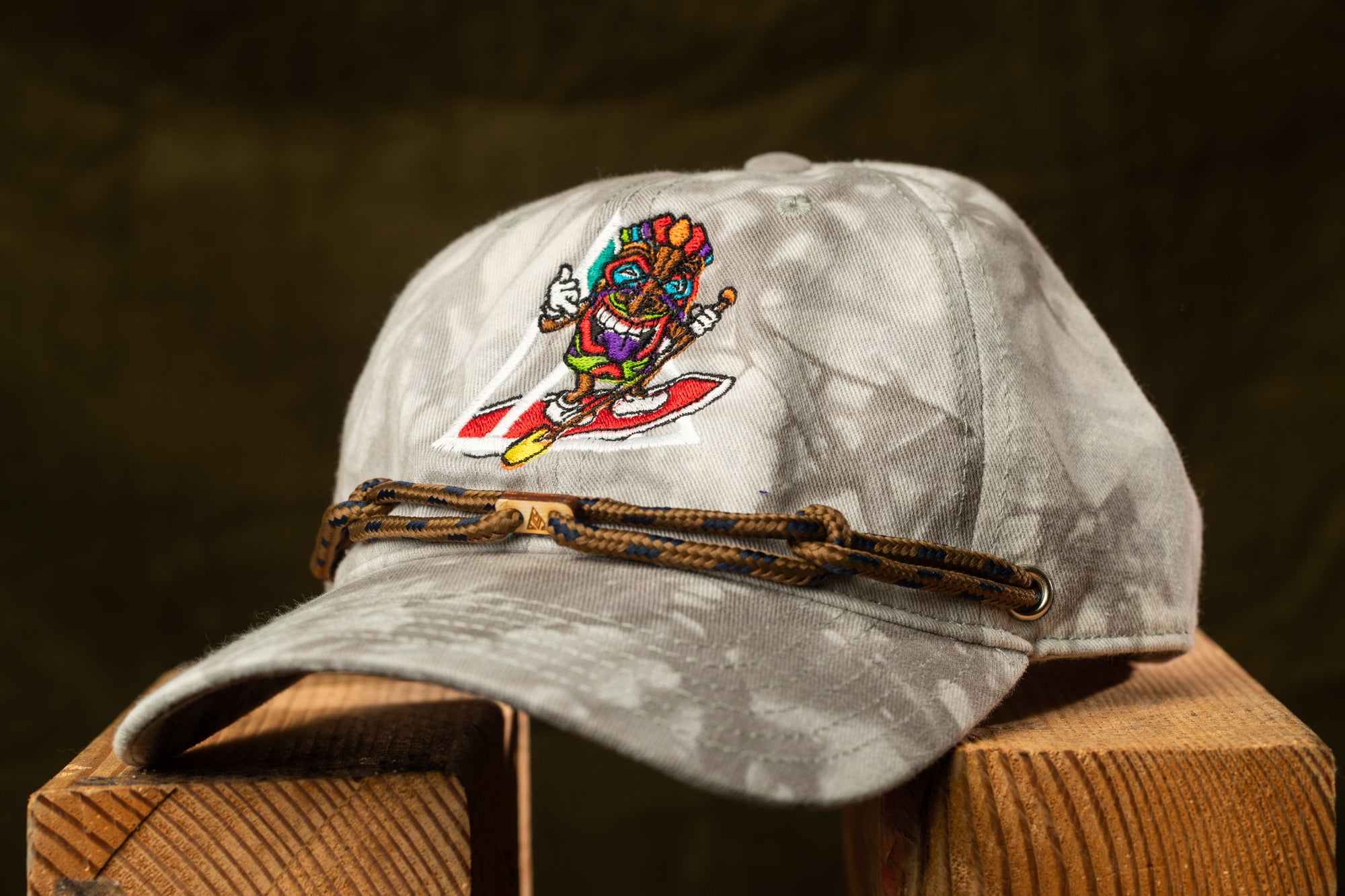A gray baseball cap with a colorful, cartoonish design on the front, featuring a character wearing a hat and holding a surfboard.