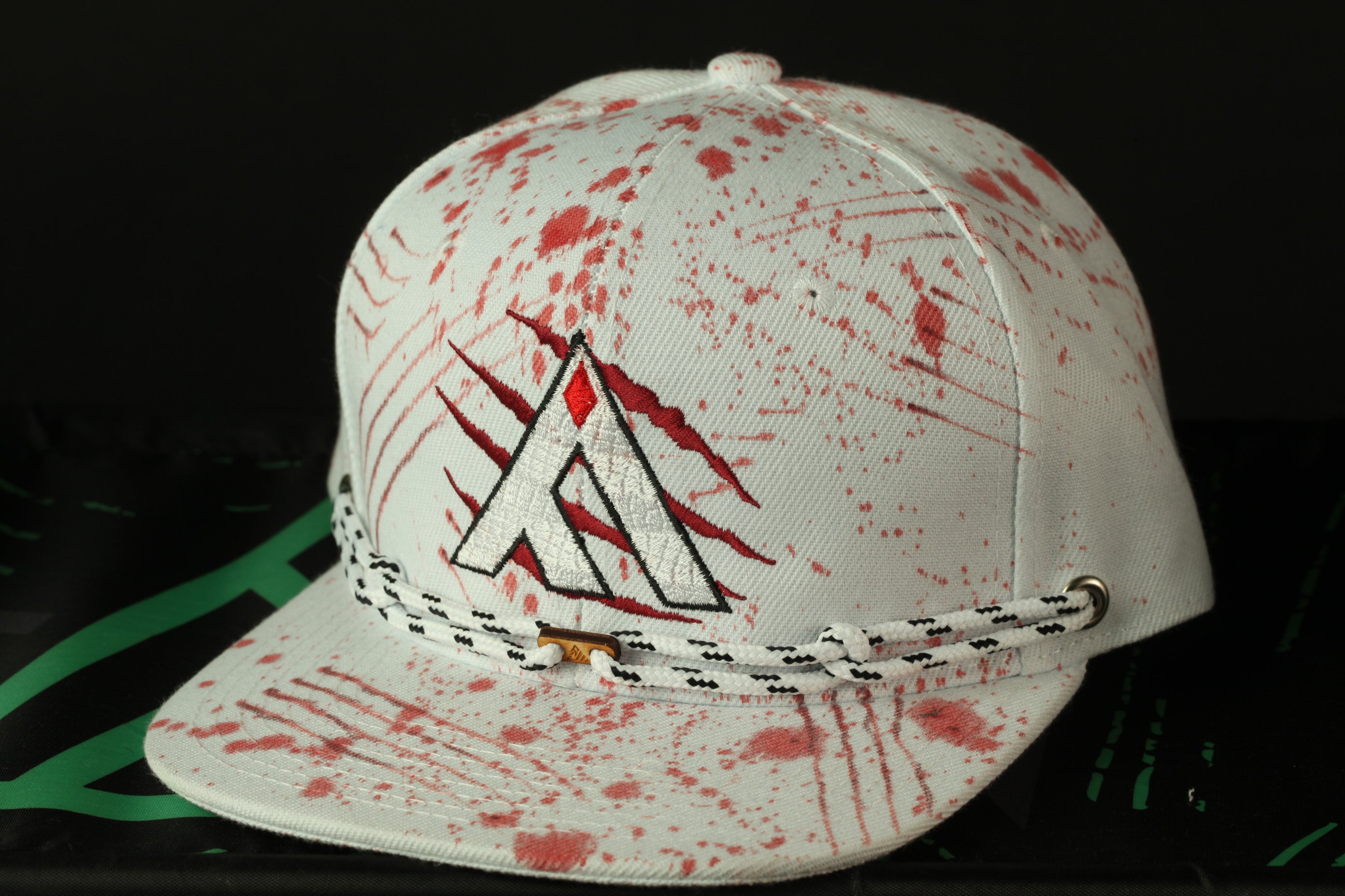 A white baseball cap with red splatters and a logo on it, placed on a black surface.