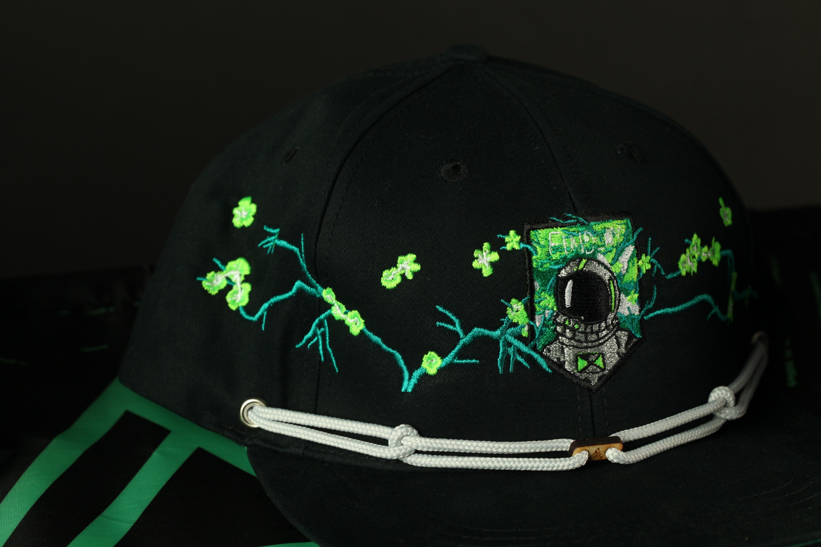A black baseball cap with a green and white floral design and a small emblem on the front.