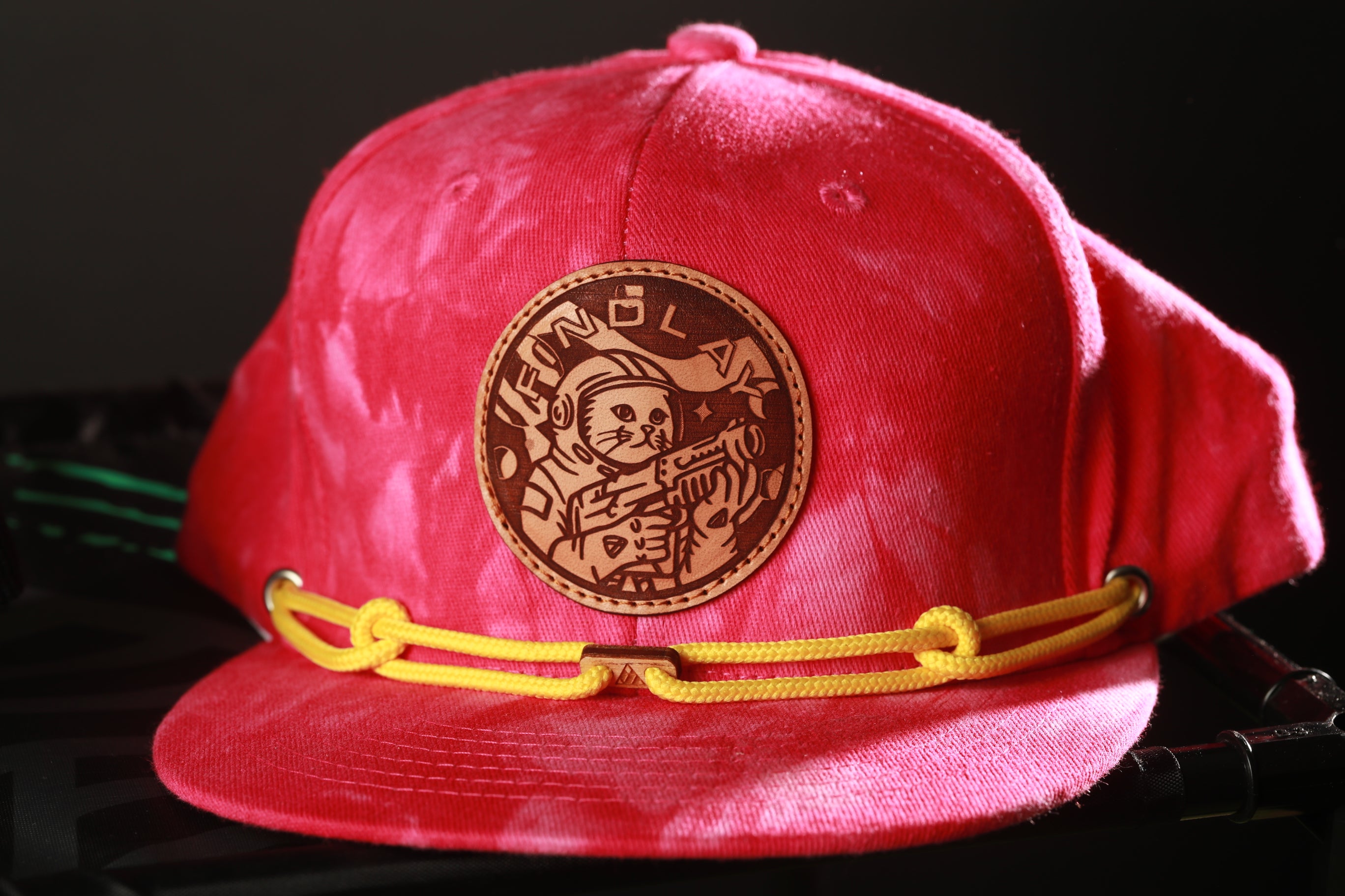A red baseball cap with a circular patch featuring a cartoon character and yellow straps.