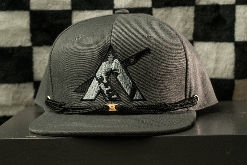 A gray baseball cap with a black and white logo on the front, sitting on a black surface against a checkered background.