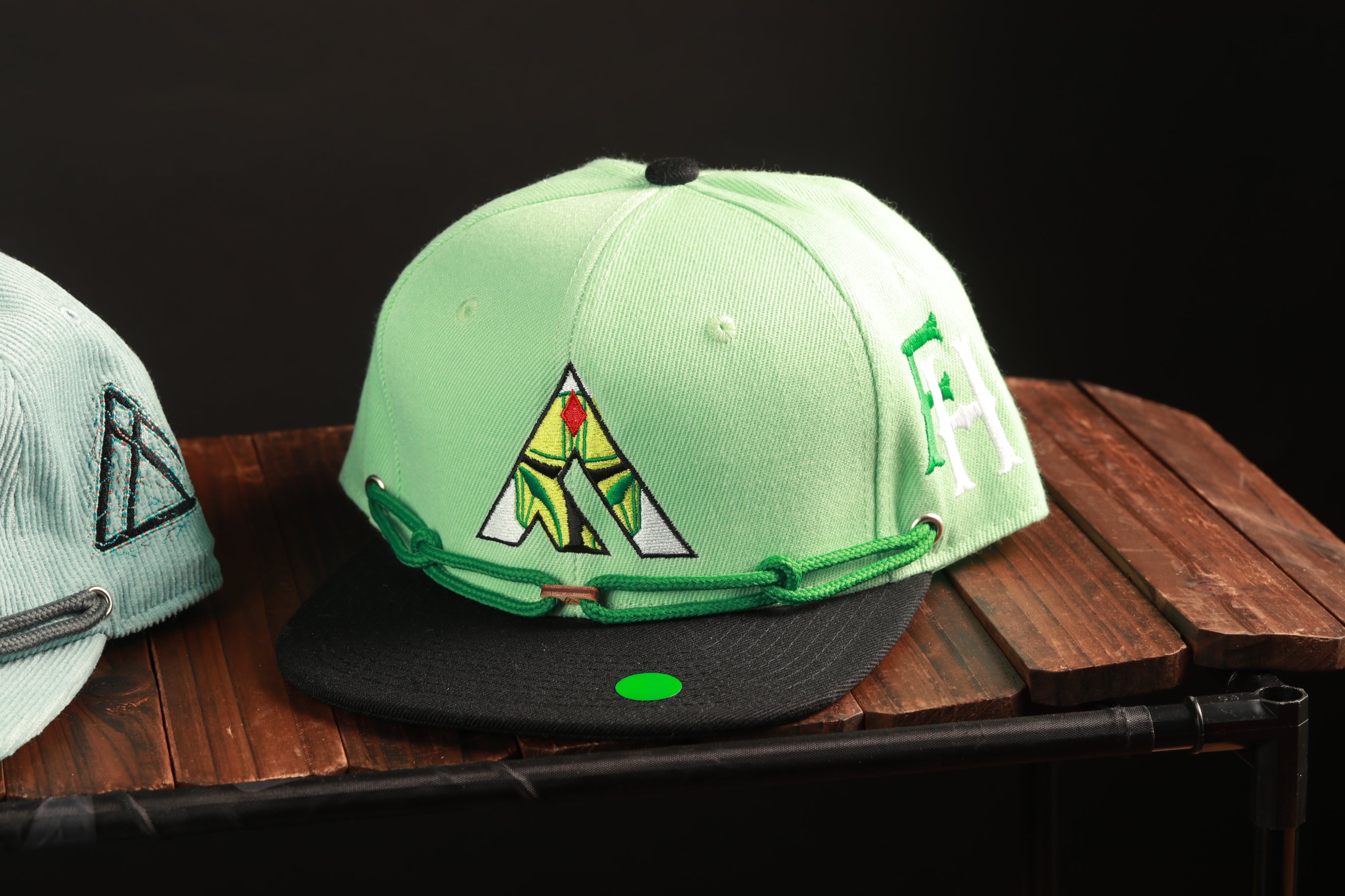 A green baseball cap with a black brim and a green chain strap is displayed on a wooden surface.