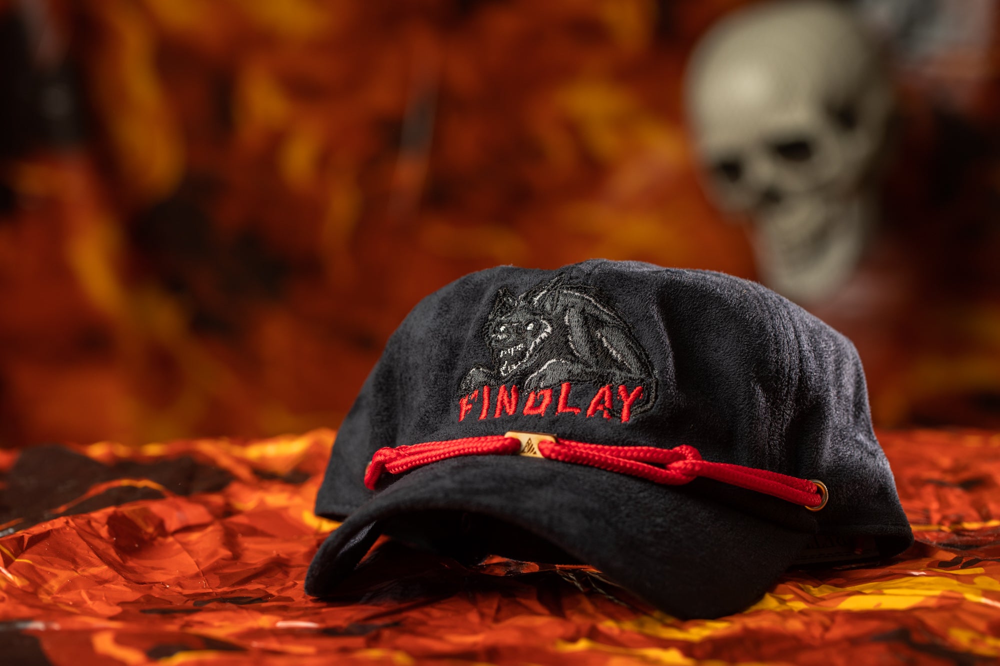 A black baseball cap with a red string and the word "FINOLAY" printed on it, placed on a red and orange background.