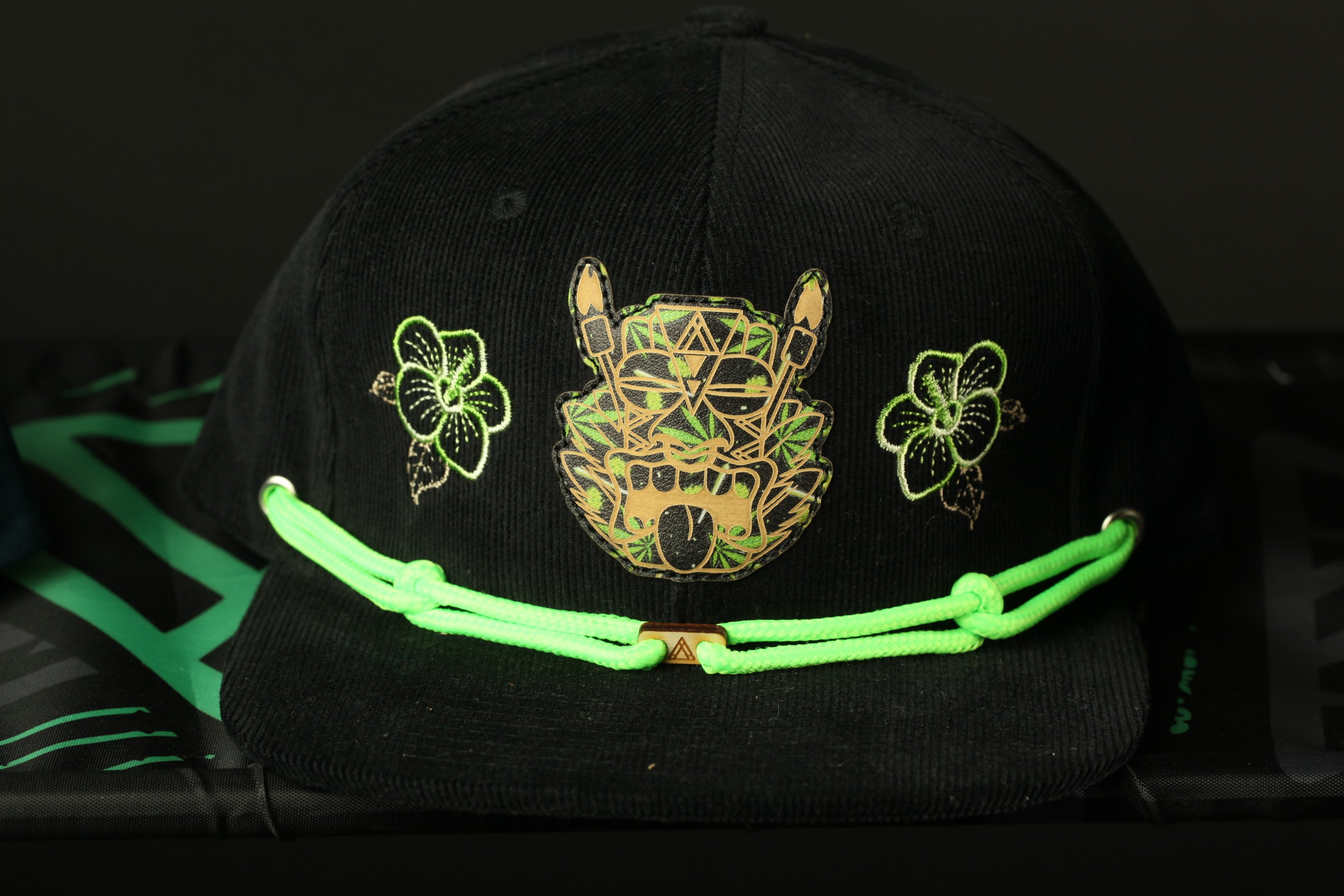 A black baseball cap with a green string and a graphic design on the front.