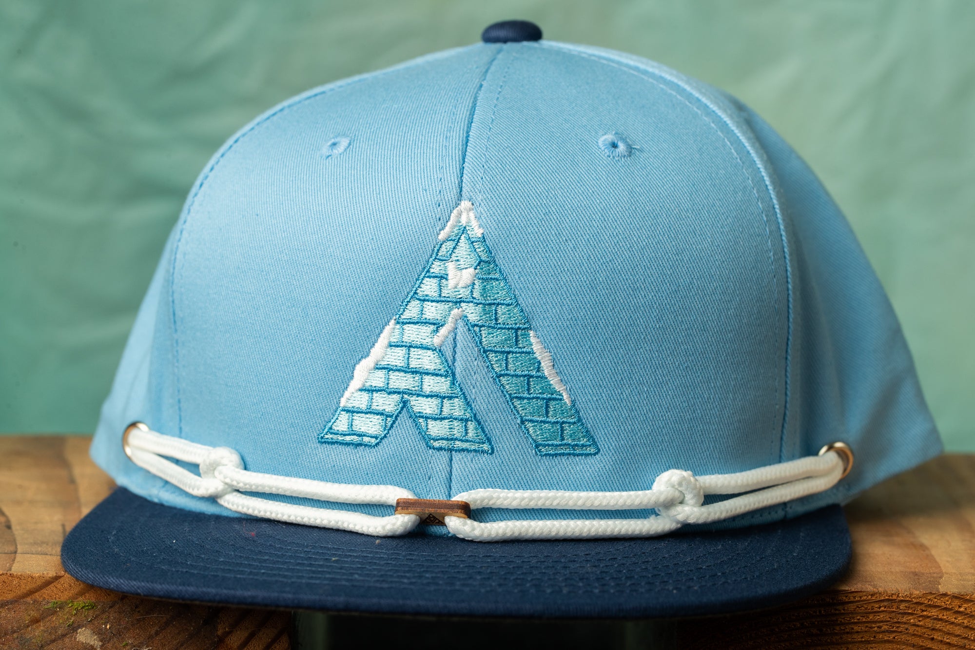 A blue baseball cap with a white rope and a blue brick pattern on the front.