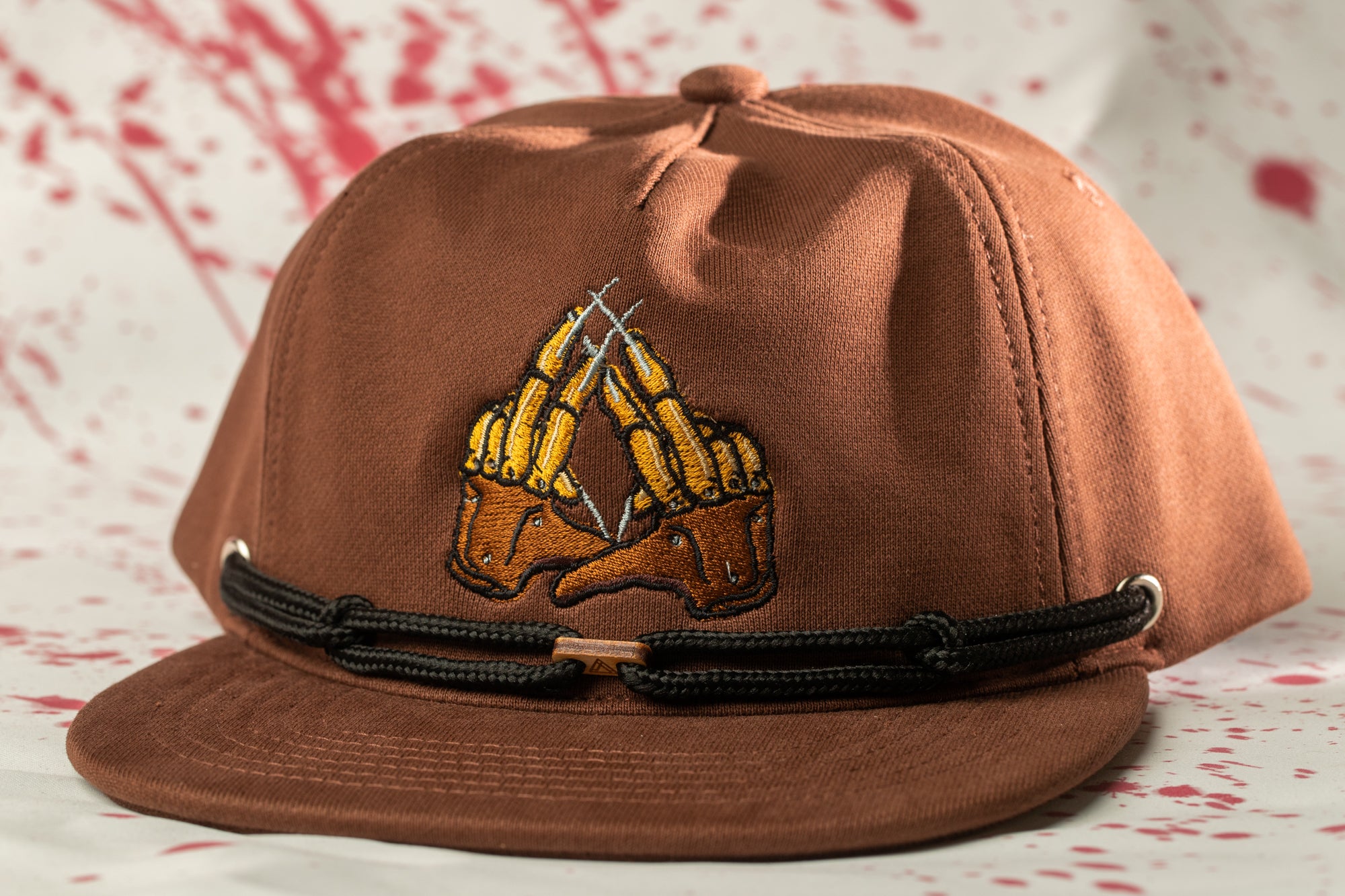 A brown baseball cap with a black band and an embroidered logo depicting a pair of claws.
