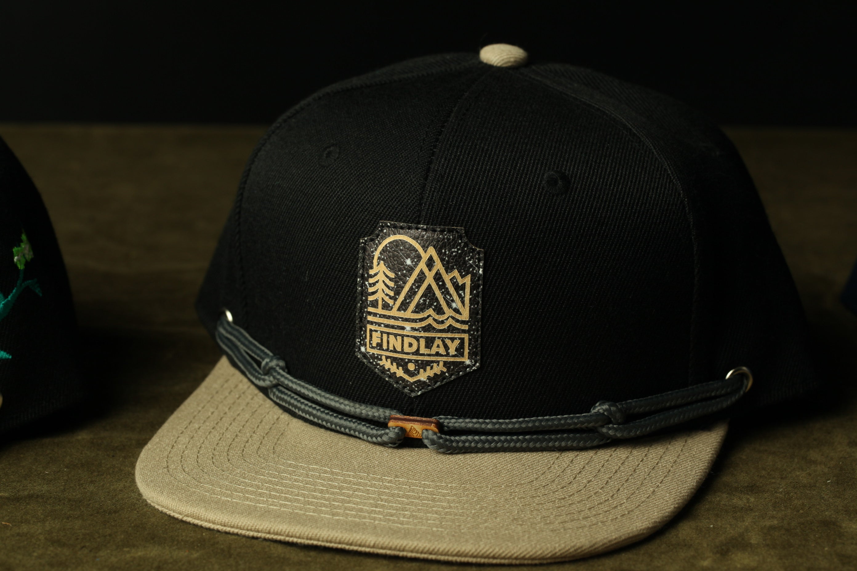 A black baseball cap with a beige brim and a logo on the front, placed on a surface.