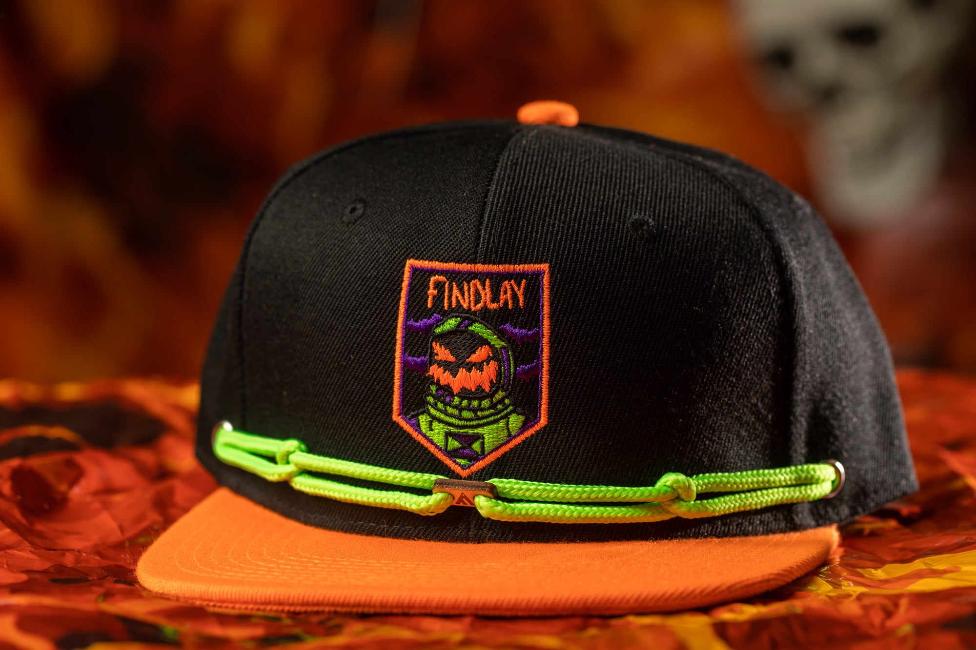 A black baseball cap with a green string and a patch featuring a cartoon character is shown against a blurred background.
