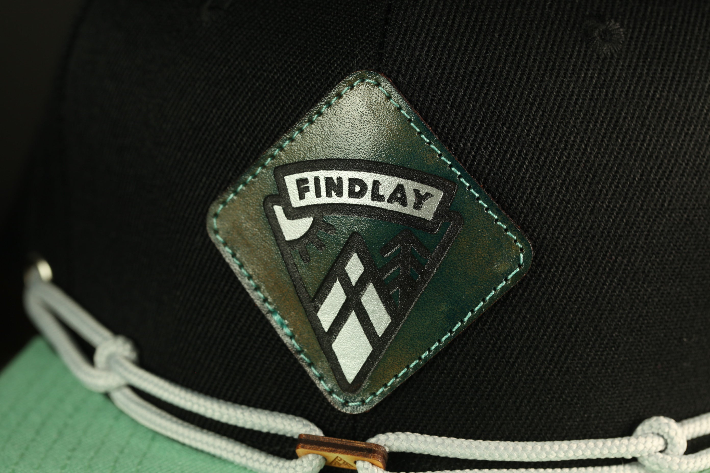 A close-up view of a black baseball cap with a green and white logo on the front.