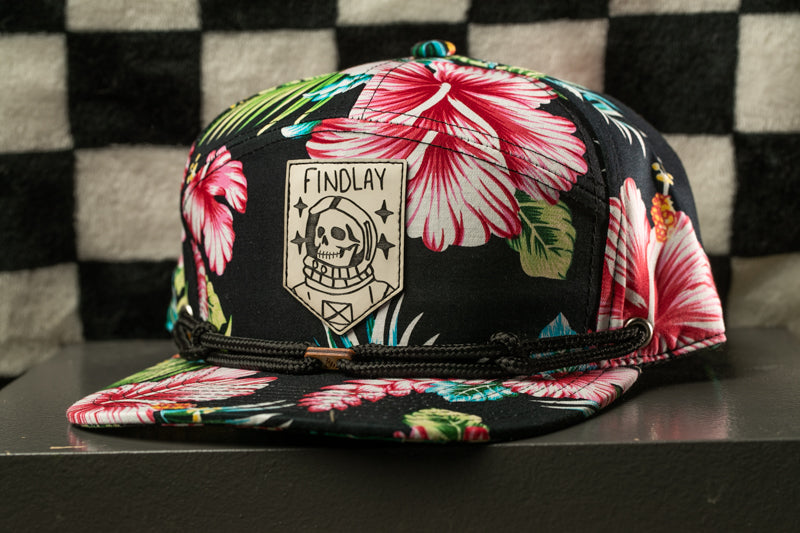 A colorful floral baseball cap with a skull and crossbones design, featuring a black band and a checkered pattern.