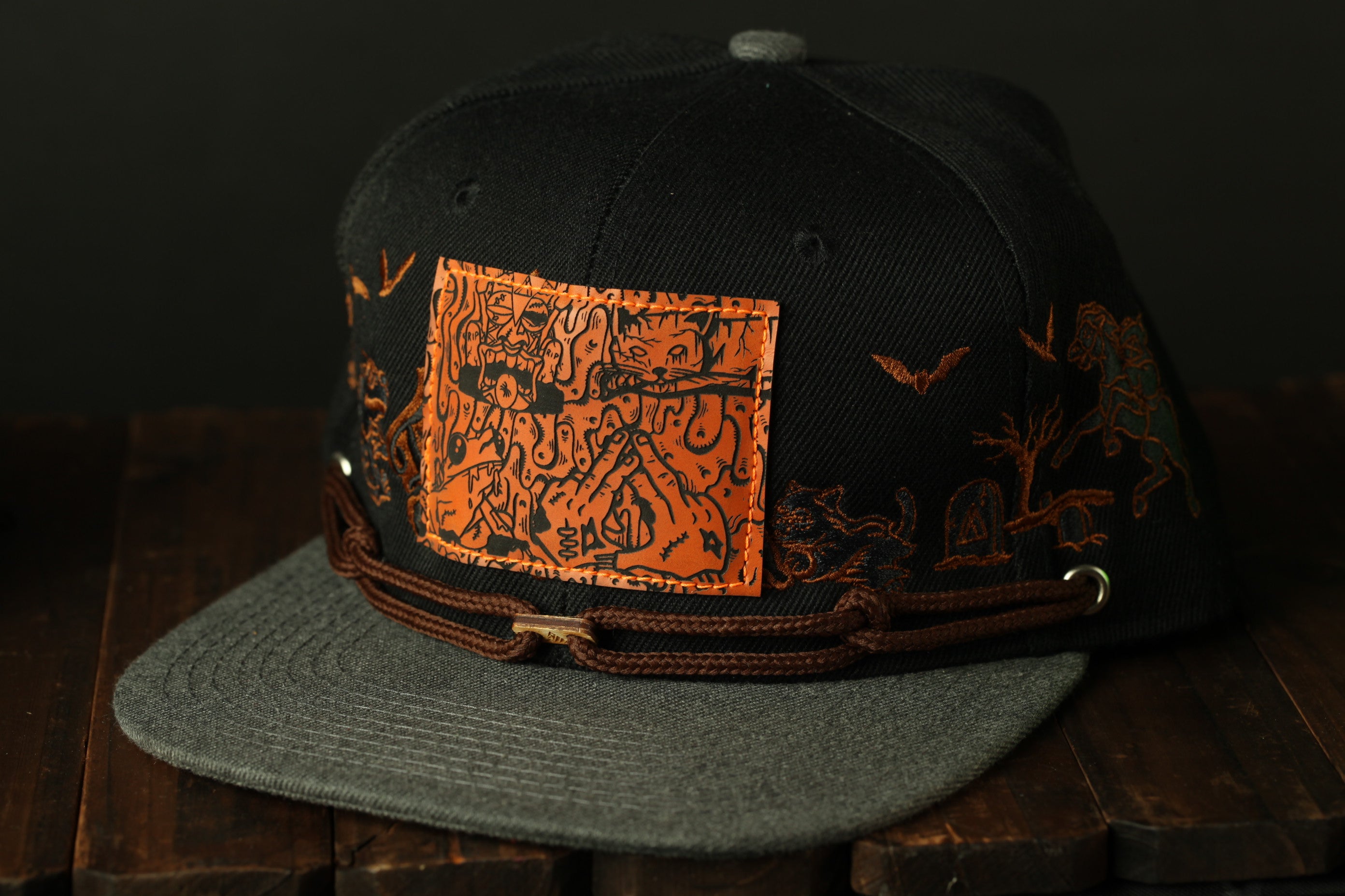 A black baseball cap with an orange patch featuring a cartoon character and bats on the front.