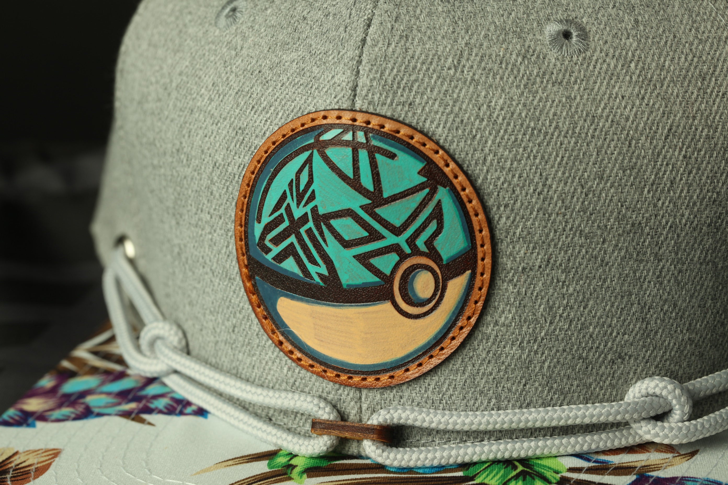 A close-up view of a gray baseball cap with a circular patch featuring a geometric design in shades of blue and brown.