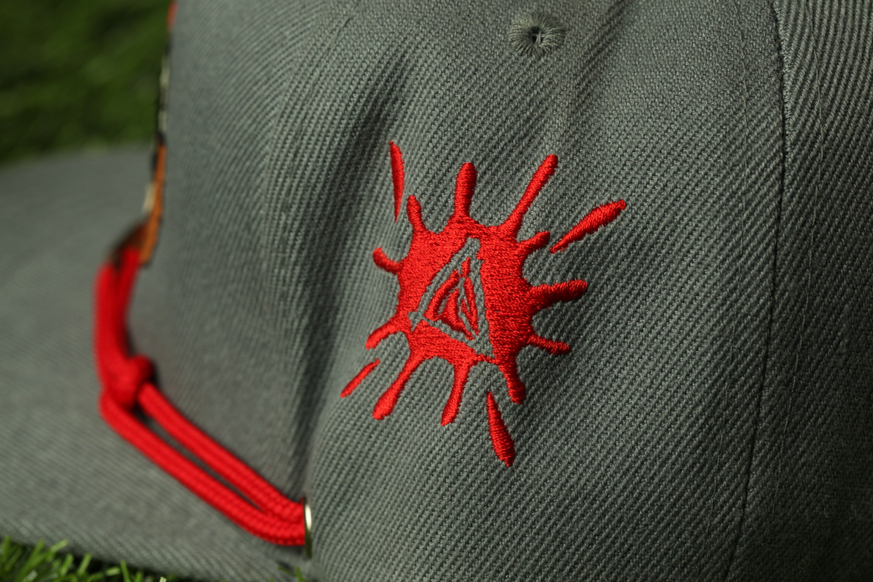 A close-up view of a gray baseball cap with a red embroidered logo on the front.