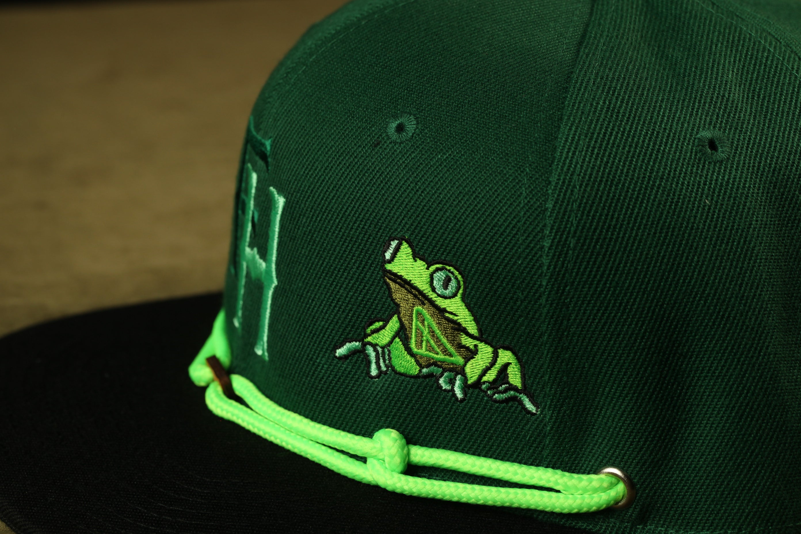 A close-up view of a green baseball cap with a frog embroidered on it.