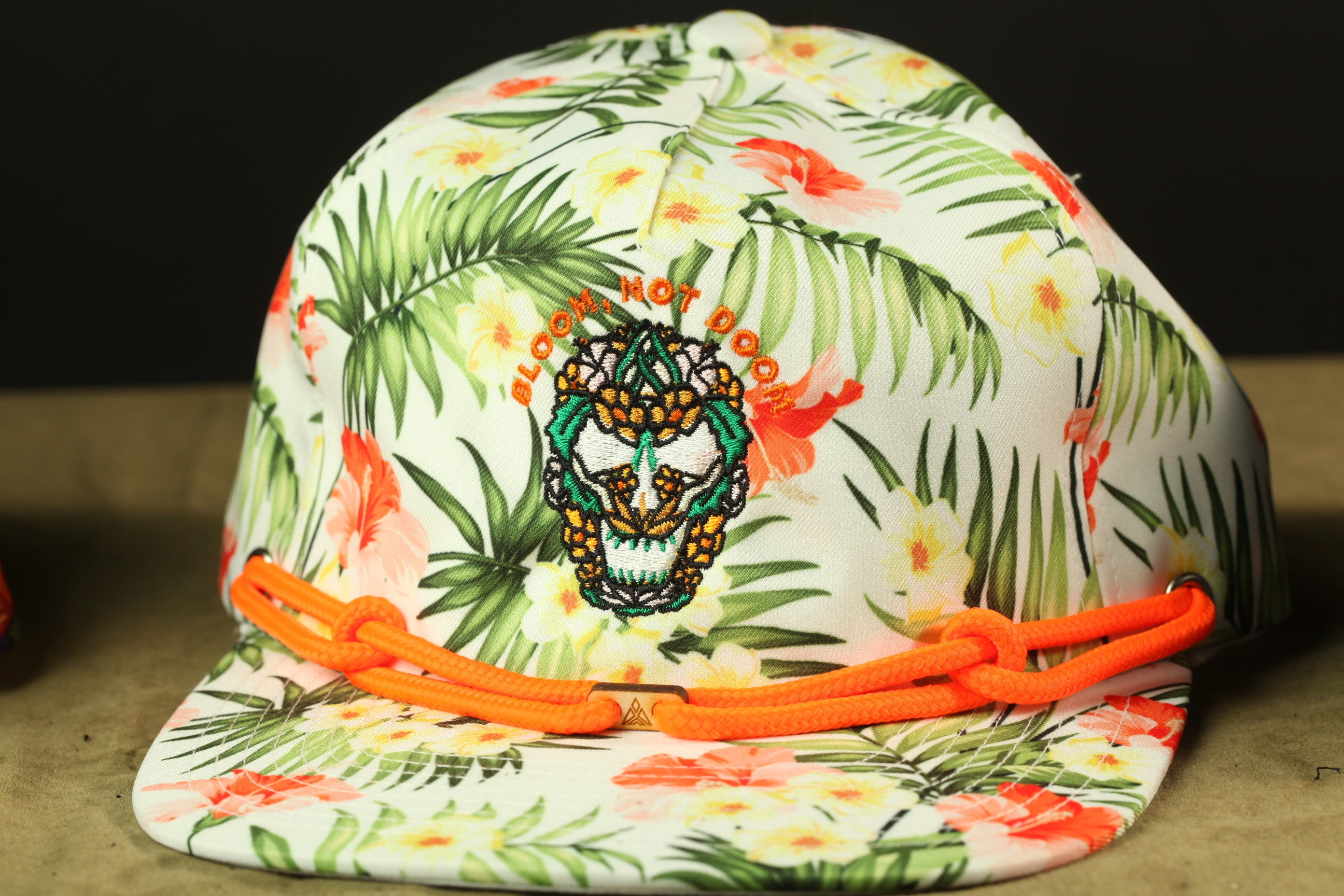 A colorful floral baseball cap with an embroidered design and orange straps.