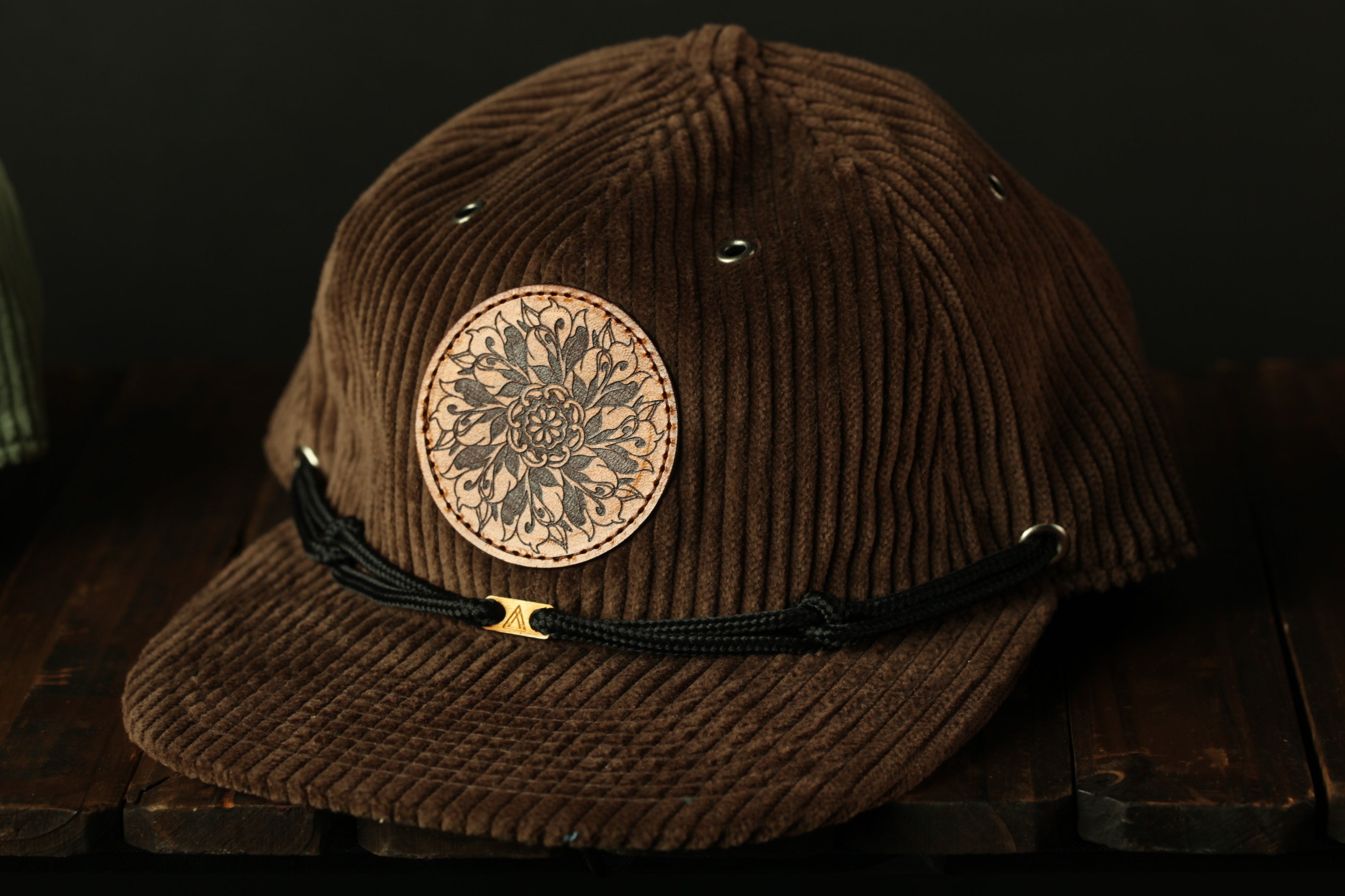 A brown corduroy baseball cap with a circular patch on the front and a black strap.