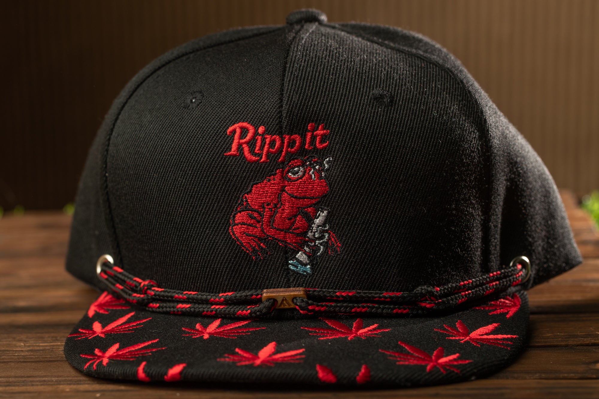 A black baseball cap with a red and black pattern, featuring a cartoon image of a frog and the word "Rippit" on the front.