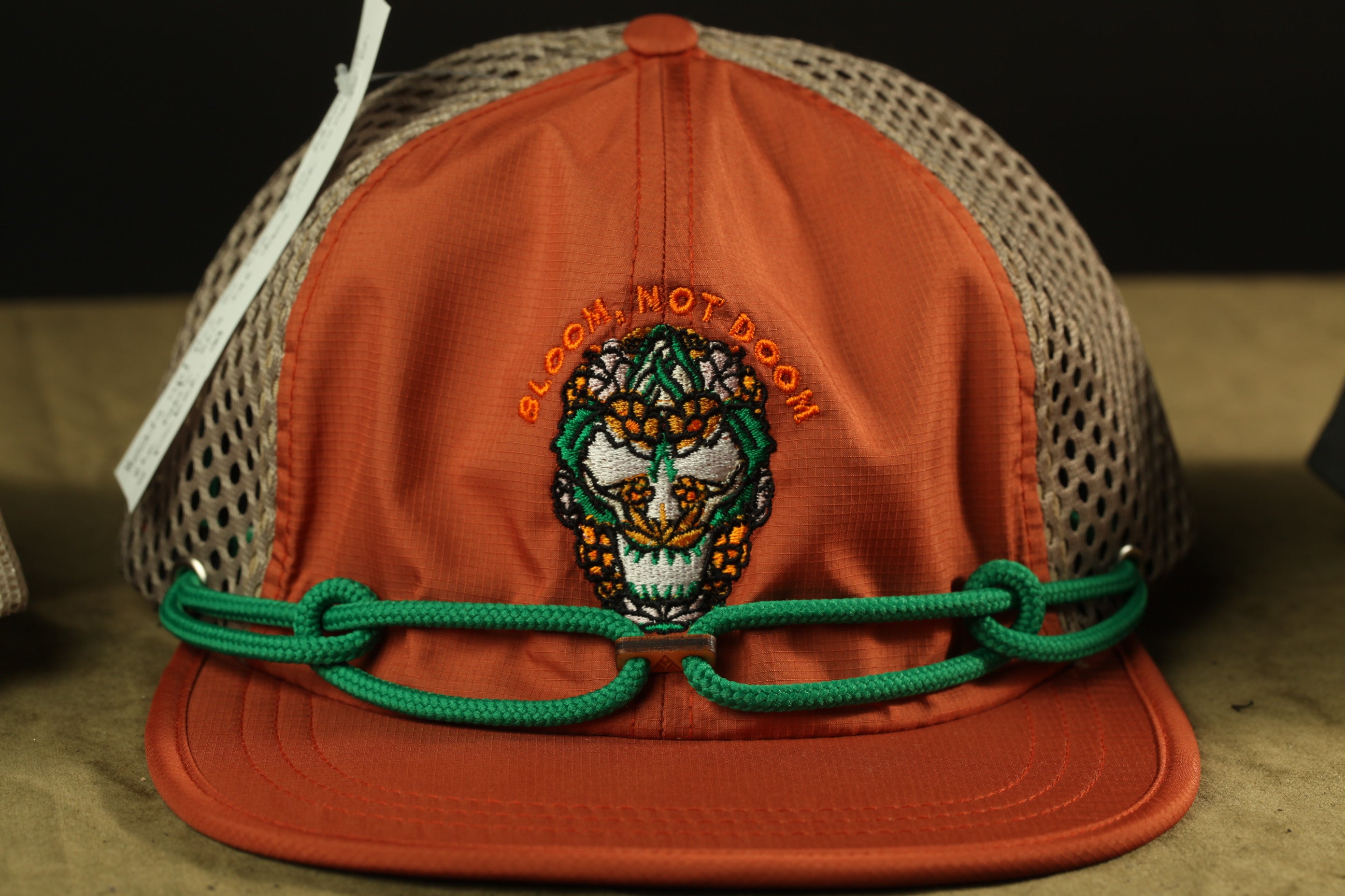 An orange baseball cap with a mesh panel and a green string.