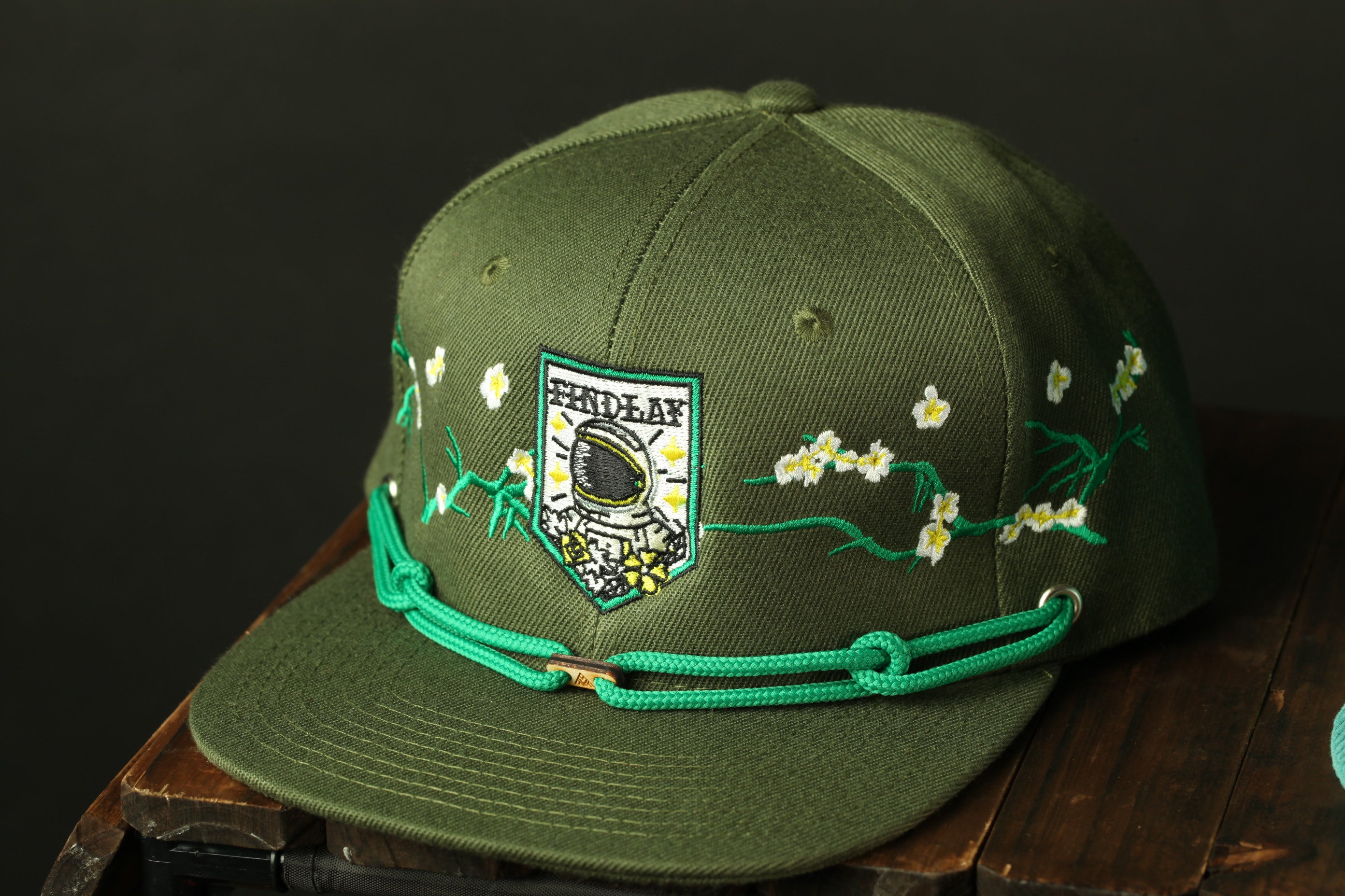 A green baseball cap with a floral design and a patch featuring a space helmet.